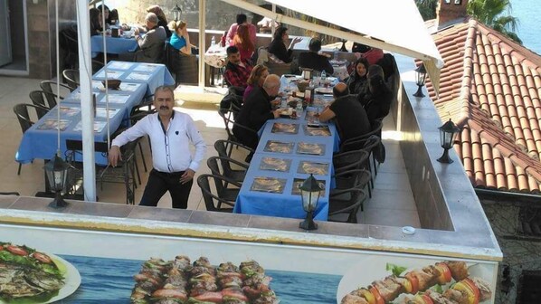 An outdoor dining area with tables covered in blue tablecloths, surrounded by chairs. - Hidirlik Pansiyon (Antalya)