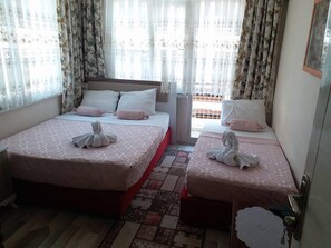 A hotel room with two beds, each with a pink bedspread and matching pillows. There is a small rug on the floor and a door with a handle. - Hidirlik Pansiyon (Antalya)
