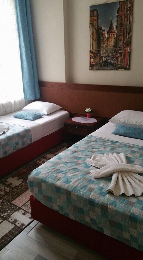 Habitación de hotel con dos camas, un cuadro de un paisaje urbano, una mesita con una flor y una alfombra estampada.