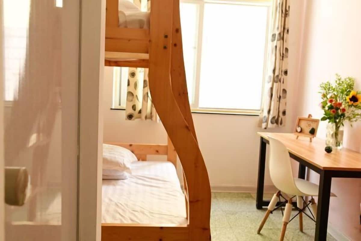 Una habitación con una cama nido, un escritorio, una silla y una ventana con cortinas.