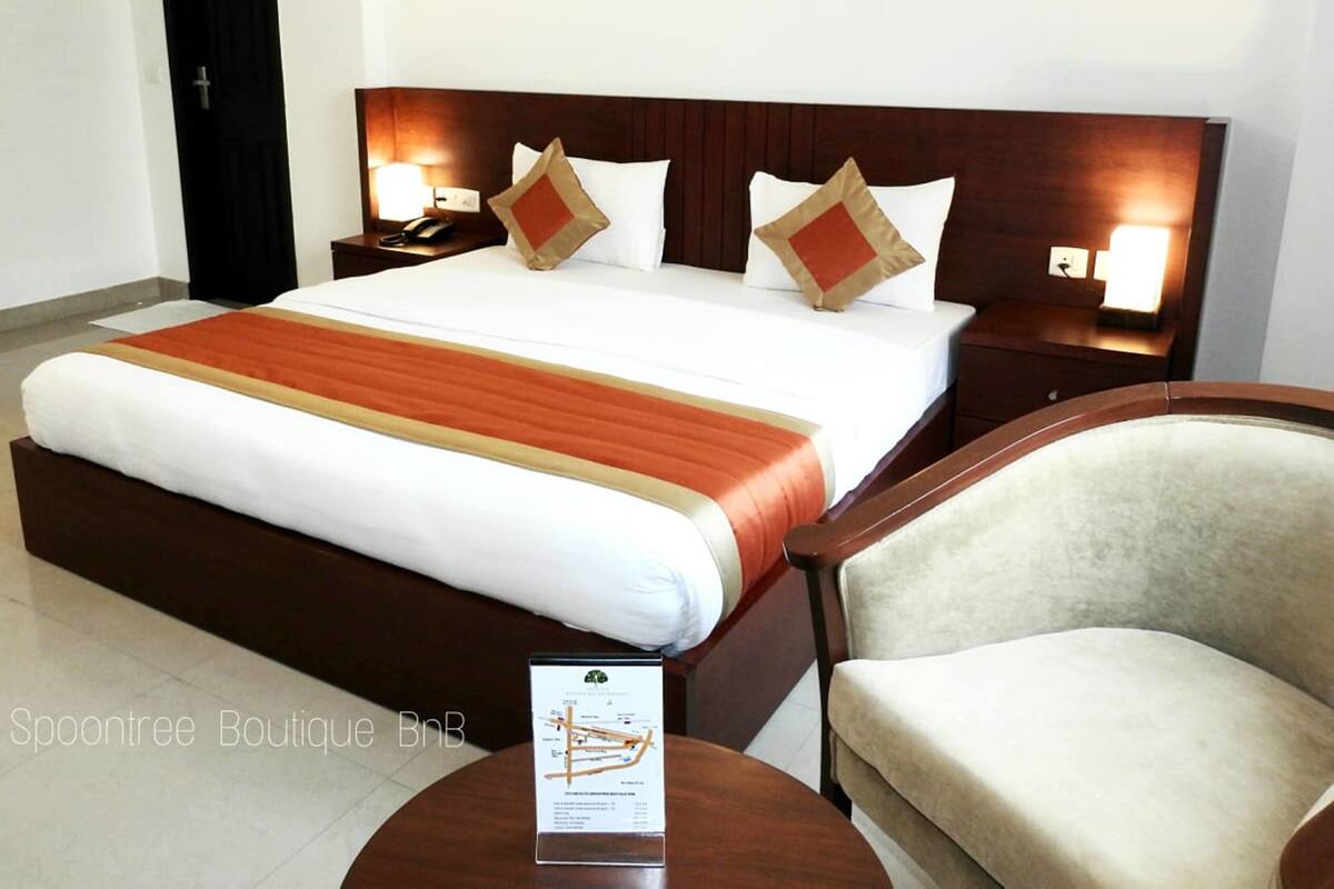 Una habitación de hotel con una cama grande, dos mesitas de noche con lámparas, una silla y un cartel sobre la mesa.