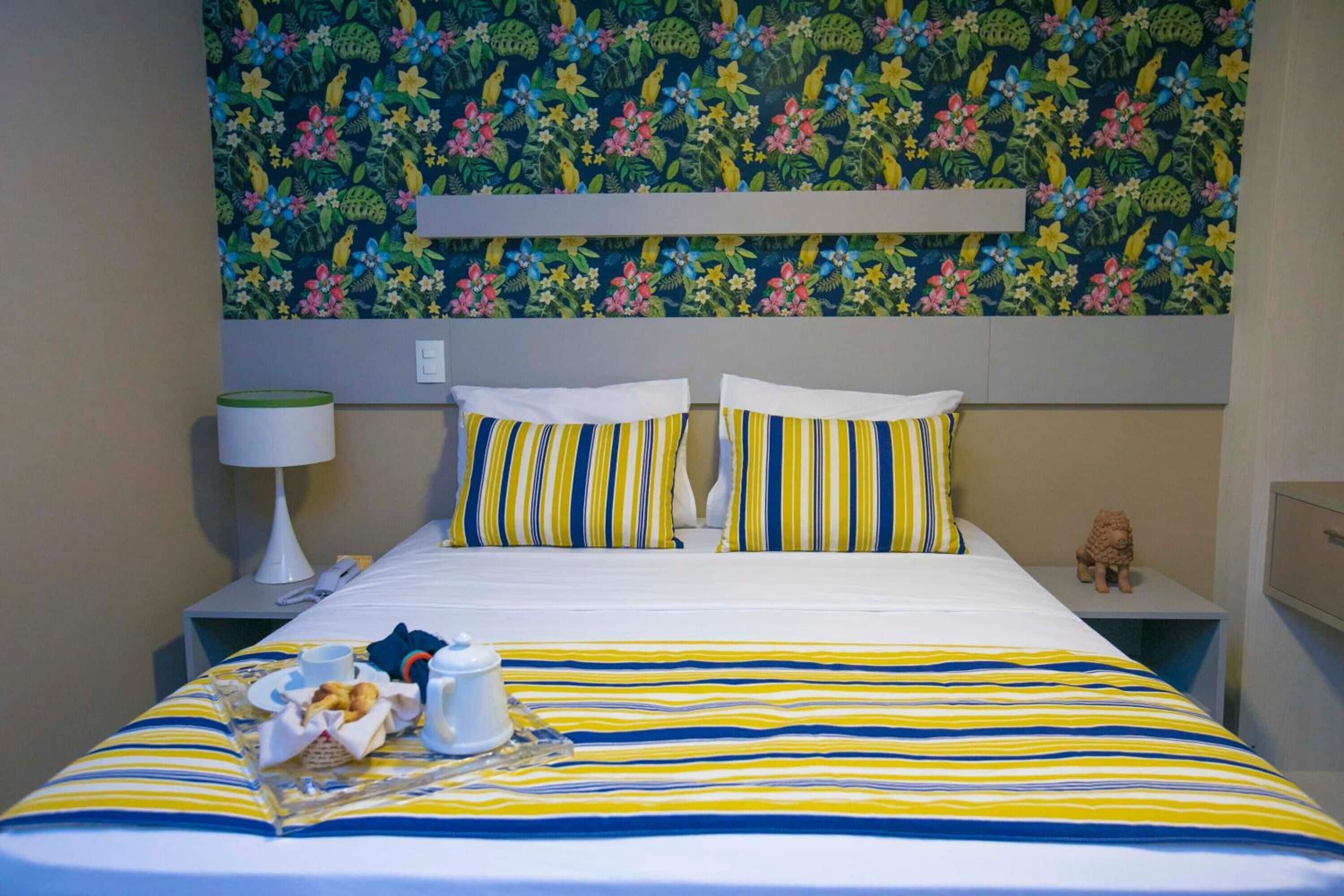 Una habitación de hotel con cama, mesita de noche, lámpara y una pared decorada con un estampado floral.