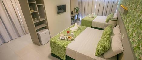 Habitación de hotel con dos camas, un escritorio, una silla, un televisor y una estantería.