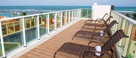 A balcony with wicker chairs, a glass balustrade, and a view of the ocean.