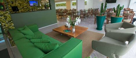 A modern hotel lobby with green seating, a wooden coffee table, and potted cacti.