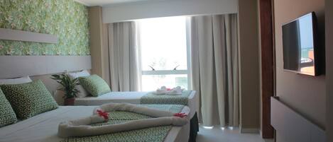 A hotel room with two beds, a TV, a potted plant, and a view of the outdoors.