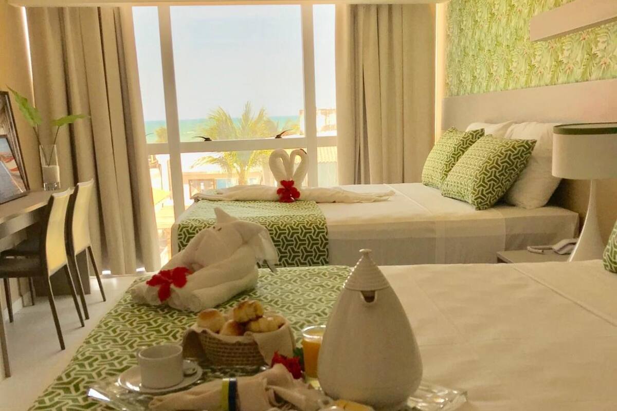 A hotel room with two beds, a dining area with breakfast, and a view of the sea.