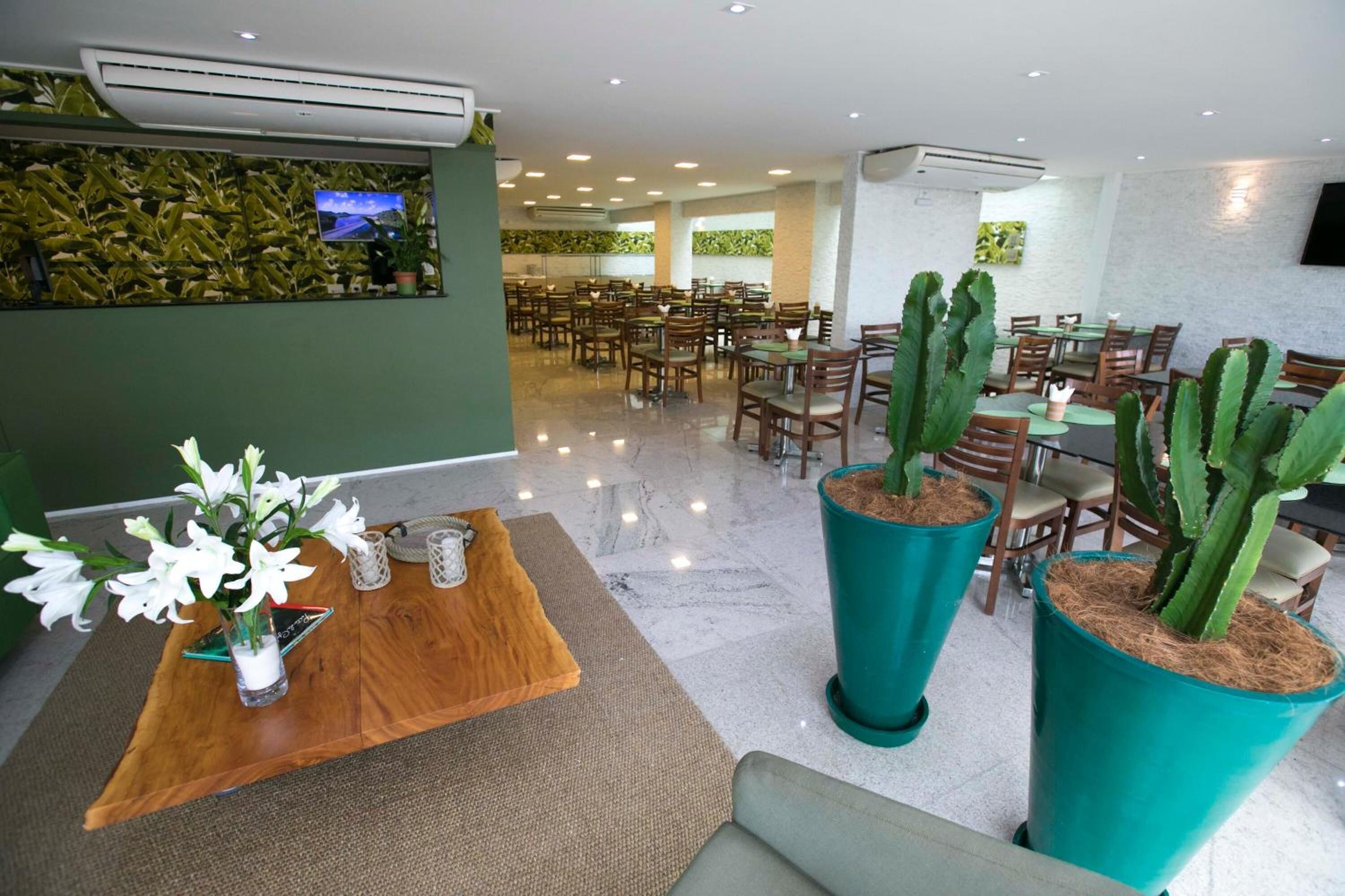 Un vaste espace dédié à la salle à manger, avec de nombreuses tables et chaises, un comptoir d’accueil agrémenté d’un vase de fleurs et de grands cactus en pot.
