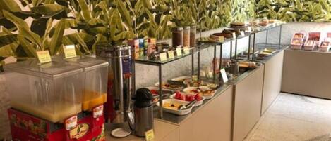 A buffet area with a variety of food items and beverages, including a fruit punch dispenser and a coffee machine.