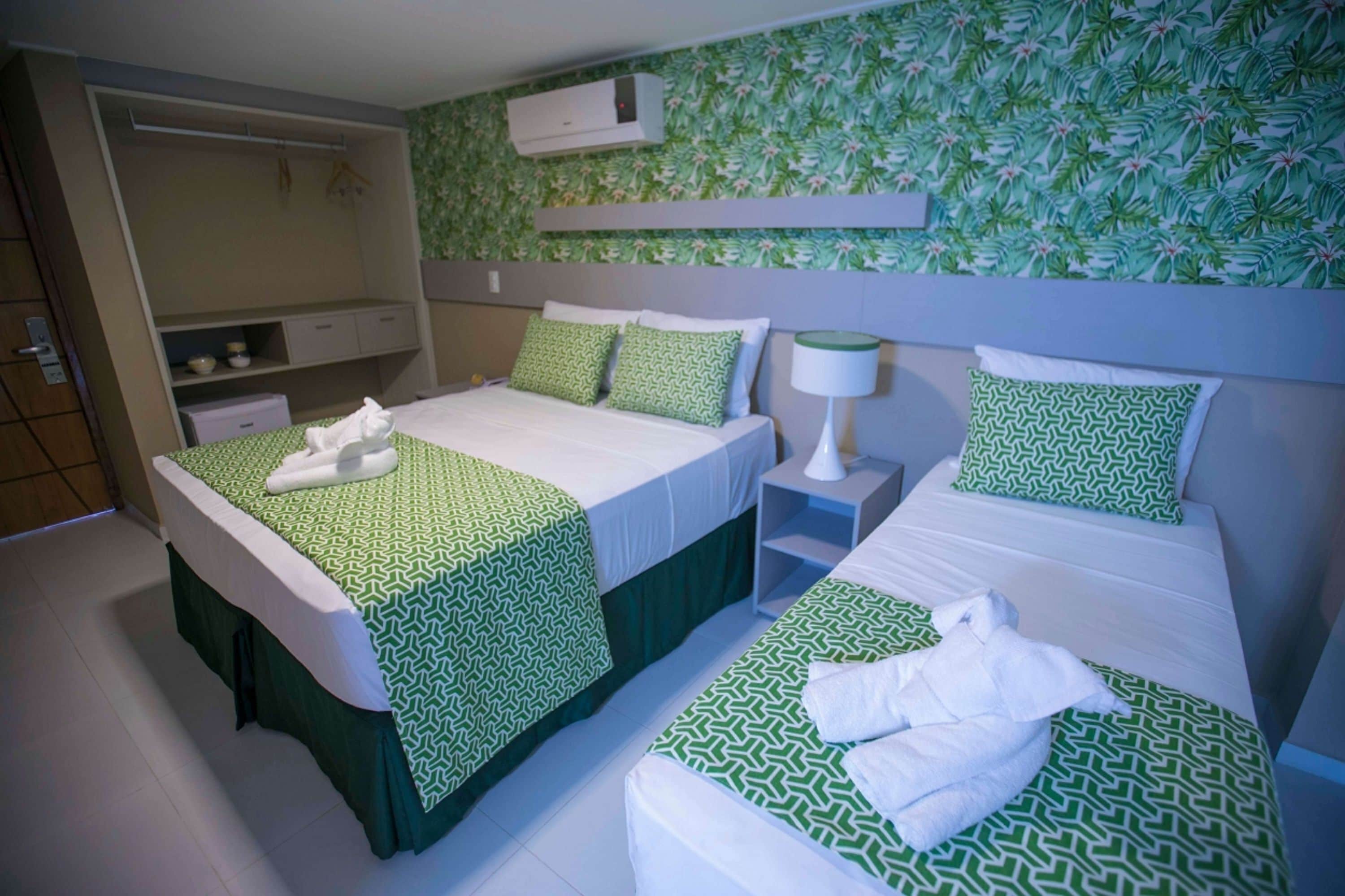 A hotel room with two beds, a wardrobe, a small desk, and a wall-mounted air conditioner.