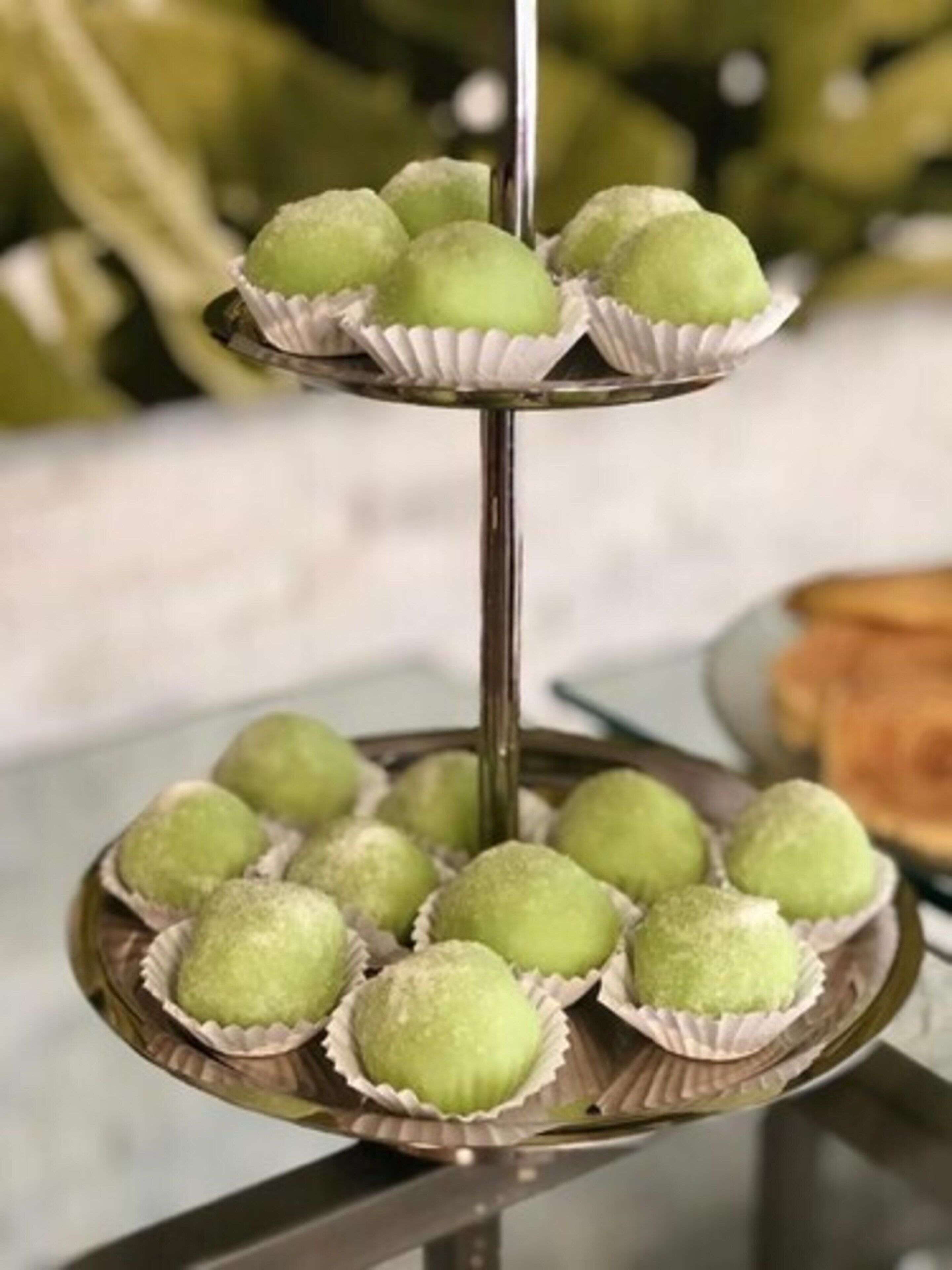 A three-tiered stand with green spherical desserts in paper cups.