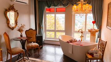 Una habitación con una bañera grande, un candelabro y vistas a árboles a través de una ventana.
