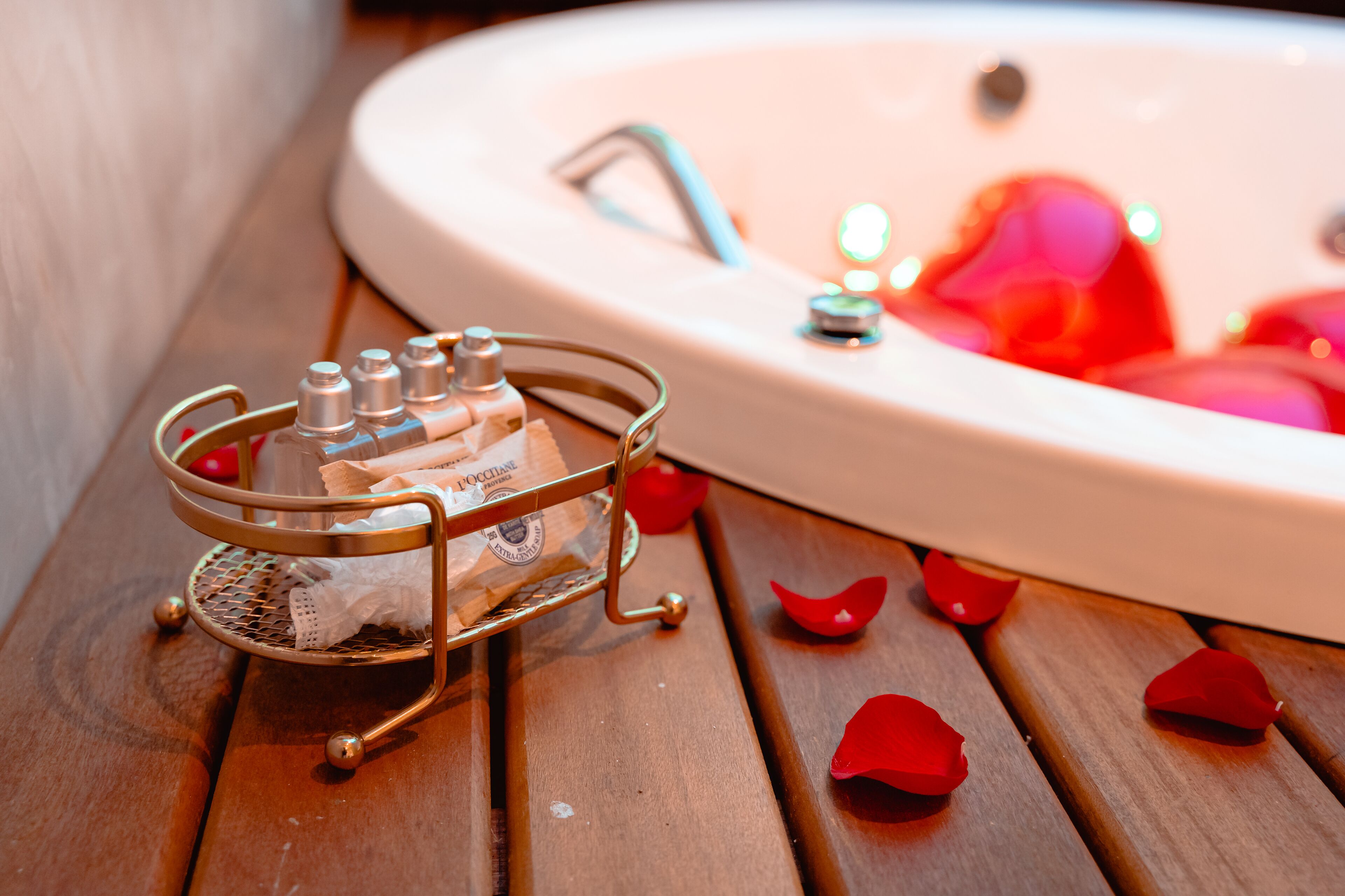 Un baño con un lavamanos, un recipiente metálico con artículos de tocador y pétalos de rosa esparcidos.