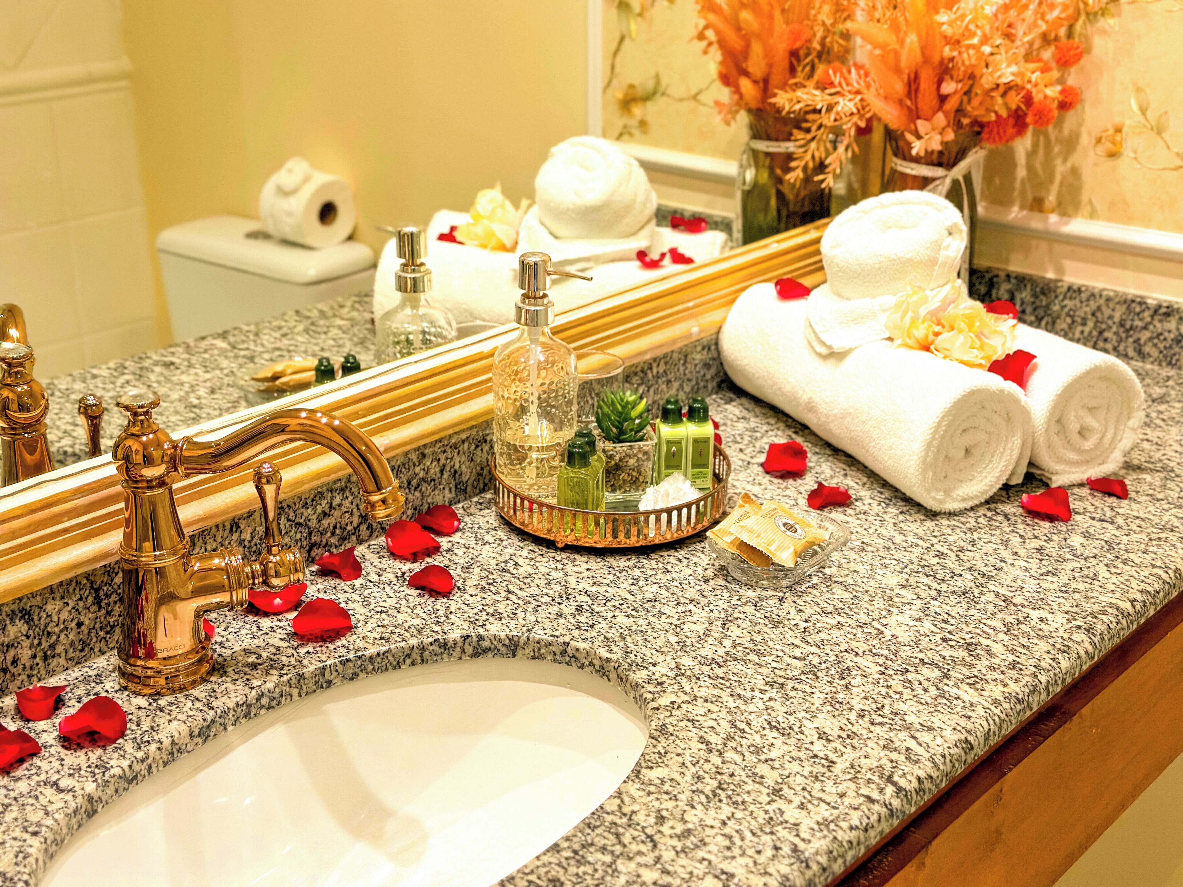 A bathroom vanity with a granite countertop, a gold faucet, and toiletries.