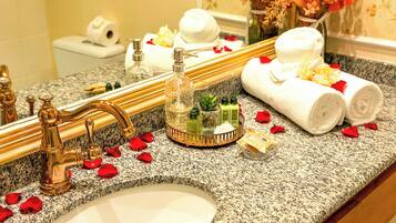 A bathroom vanity with a granite countertop, a gold faucet, and toiletries.