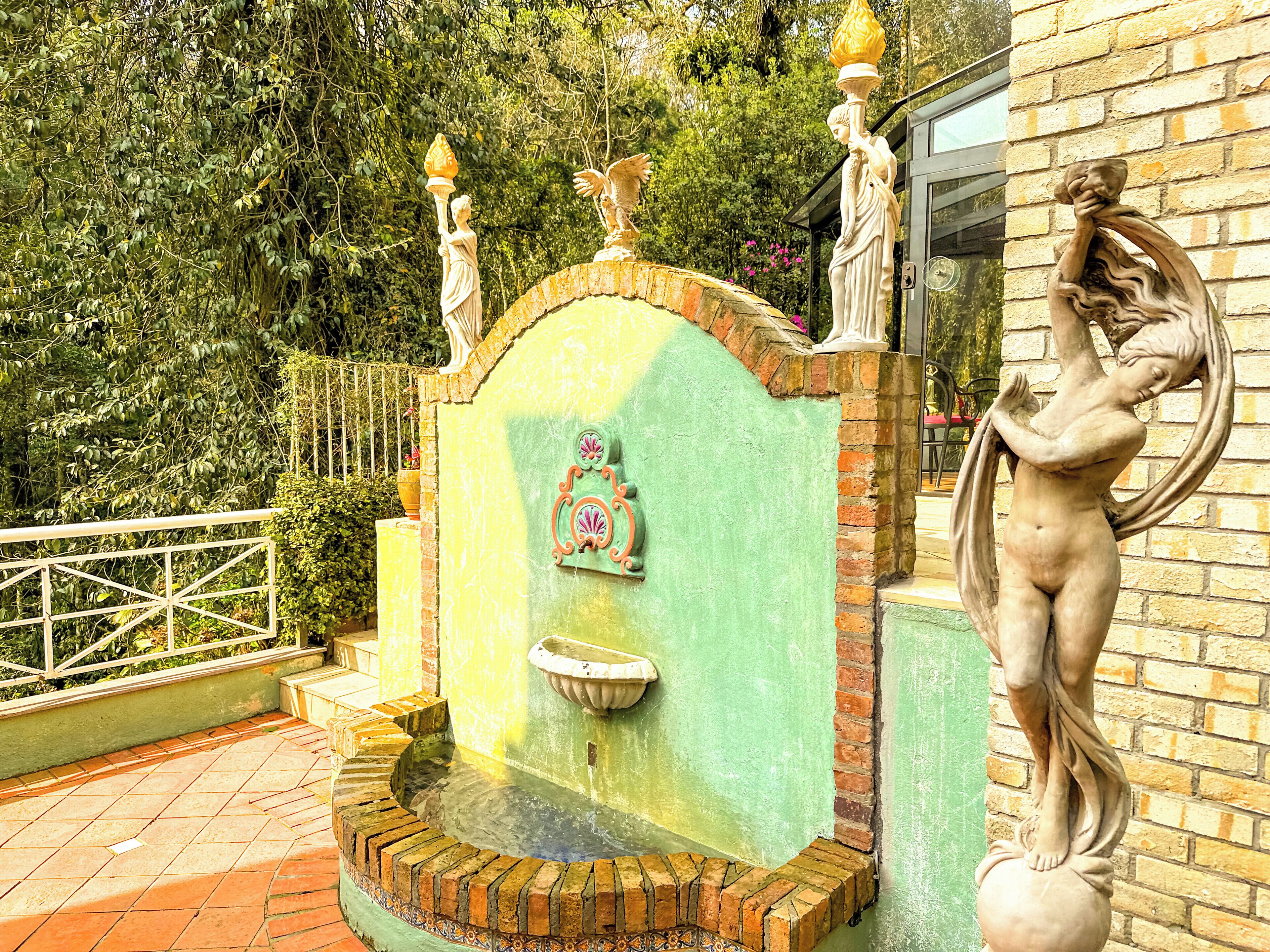 A fountain with a statue of a woman holding a torch, surrounded by greenery.