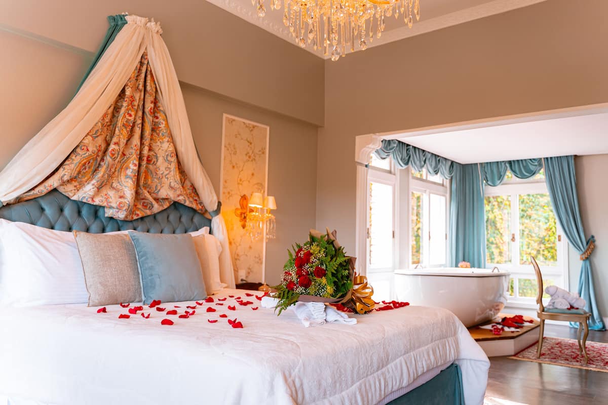 A luxurious bedroom with a canopy bed, a decorative floral arrangement, and a bathtub.