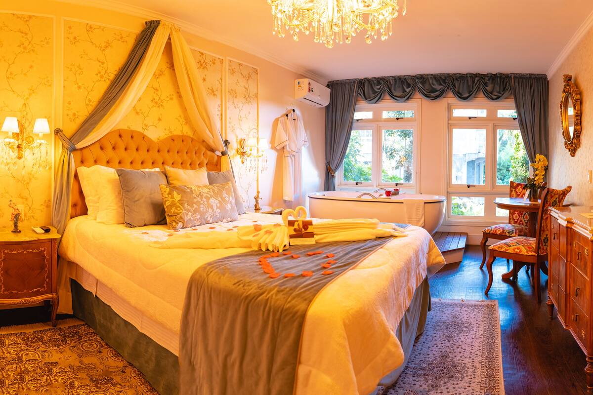 A spacious bedroom with a large bed, a sitting area with a chair, and a view of the outdoors through the windows.