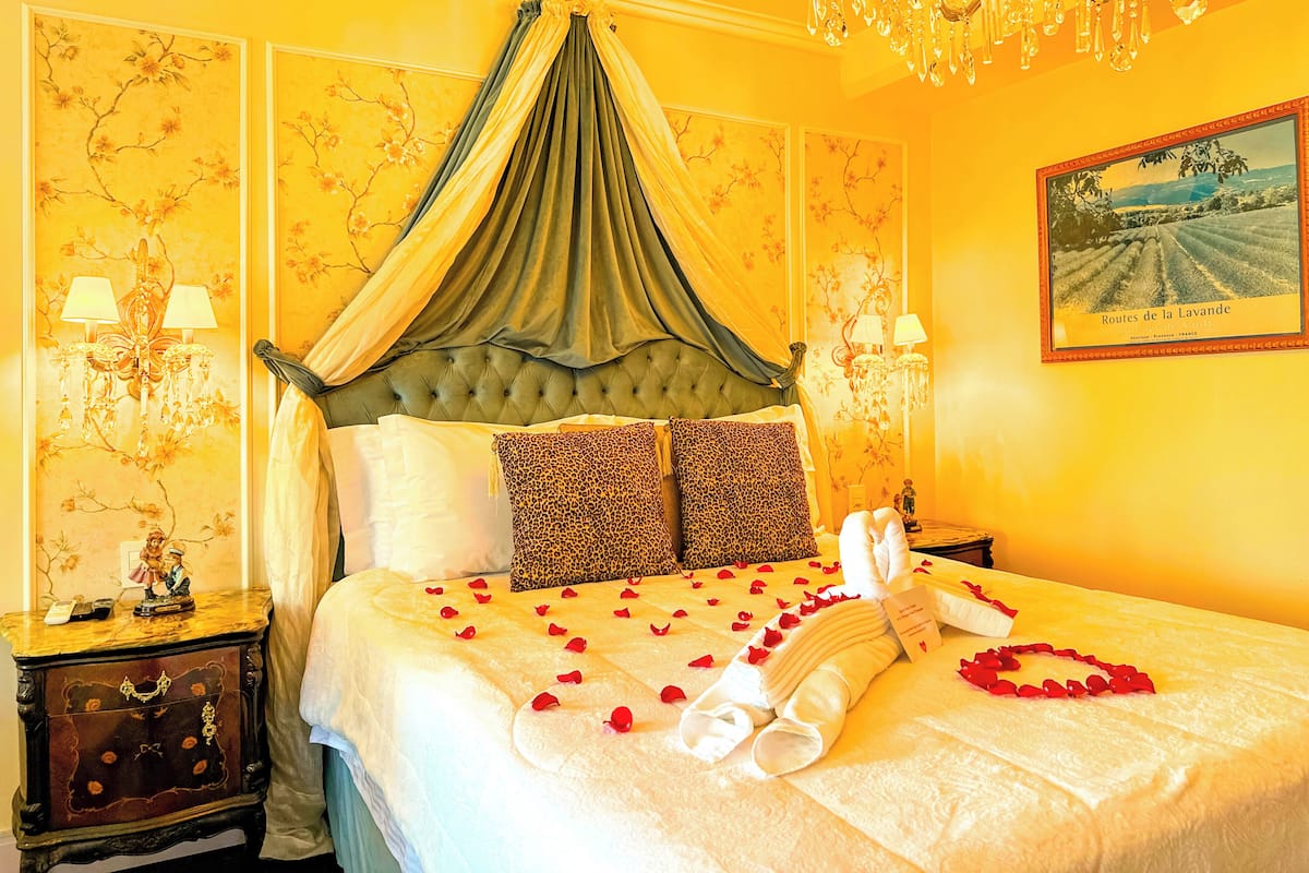 A luxurious bedroom with a canopy bed, floral wallpaper, and a chandelier.