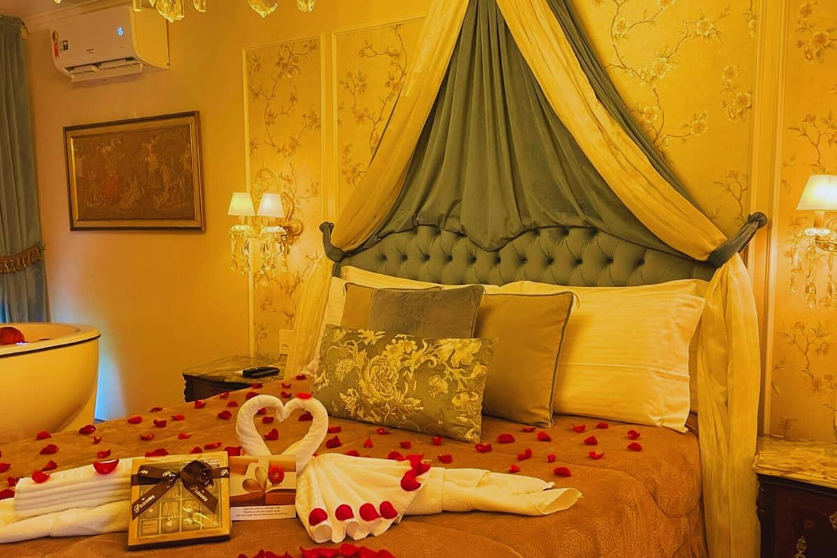 A luxurious bedroom with a canopy bed, floral wallpaper, and rose petals arranged on the bed.