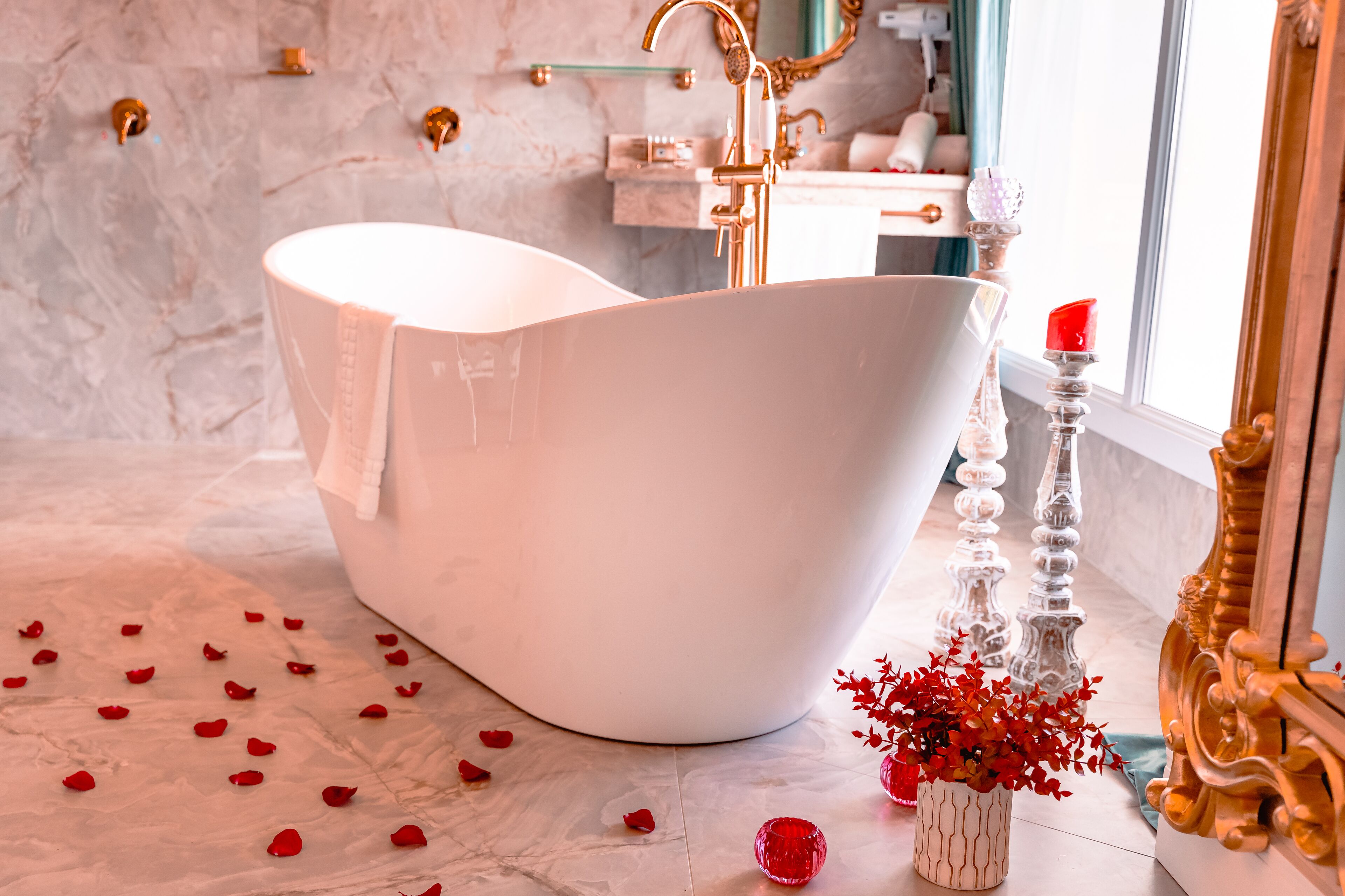 Un baño moderno con una bañera independiente, suelo de mármol y detalles decorativos como flores rojas y velas.