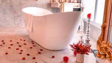 Un baño moderno con una bañera independiente, suelo de mármol y detalles decorativos como flores rojas y velas.