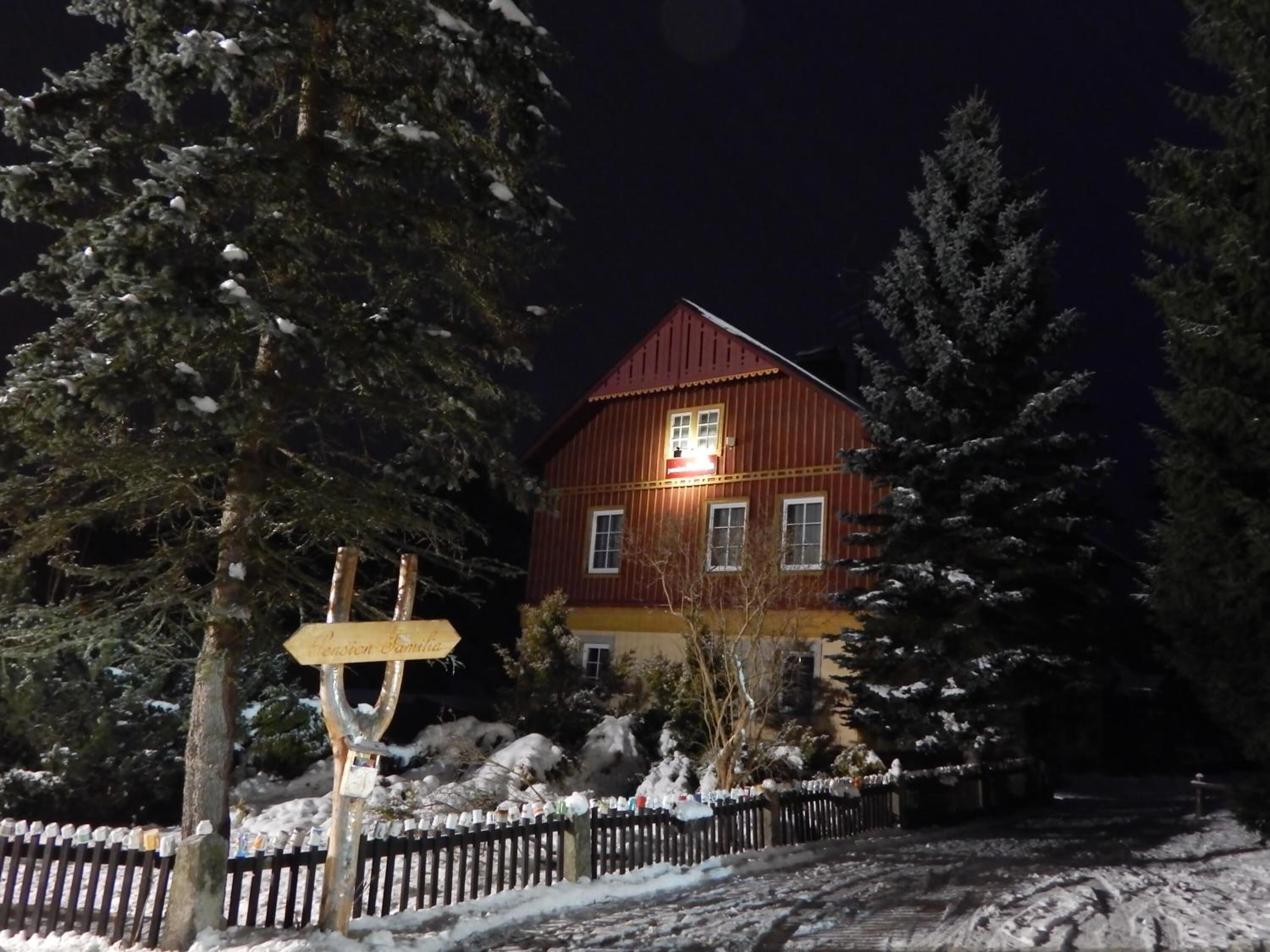 Une maison en bois avec un toit rouge, entourée d’arbres couverts de neige et d’une clôture en bois.