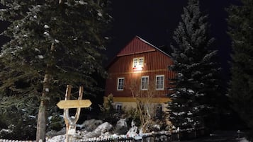 Une maison en bois avec un toit rouge, entourée d’arbres couverts de neige et d’une clôture en bois.