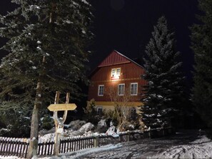 A wooden house with a red roof, surrounded by snow-covered trees and a wooden fence. - Pension Familia (Harrachov)