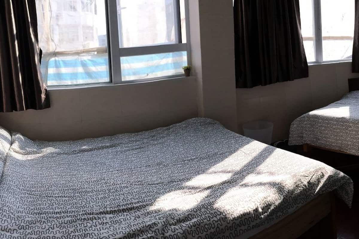 Une chambre avec deux lits, une fenêtre avec des rideaux et une petite plante sur le rebord de la fenêtre.