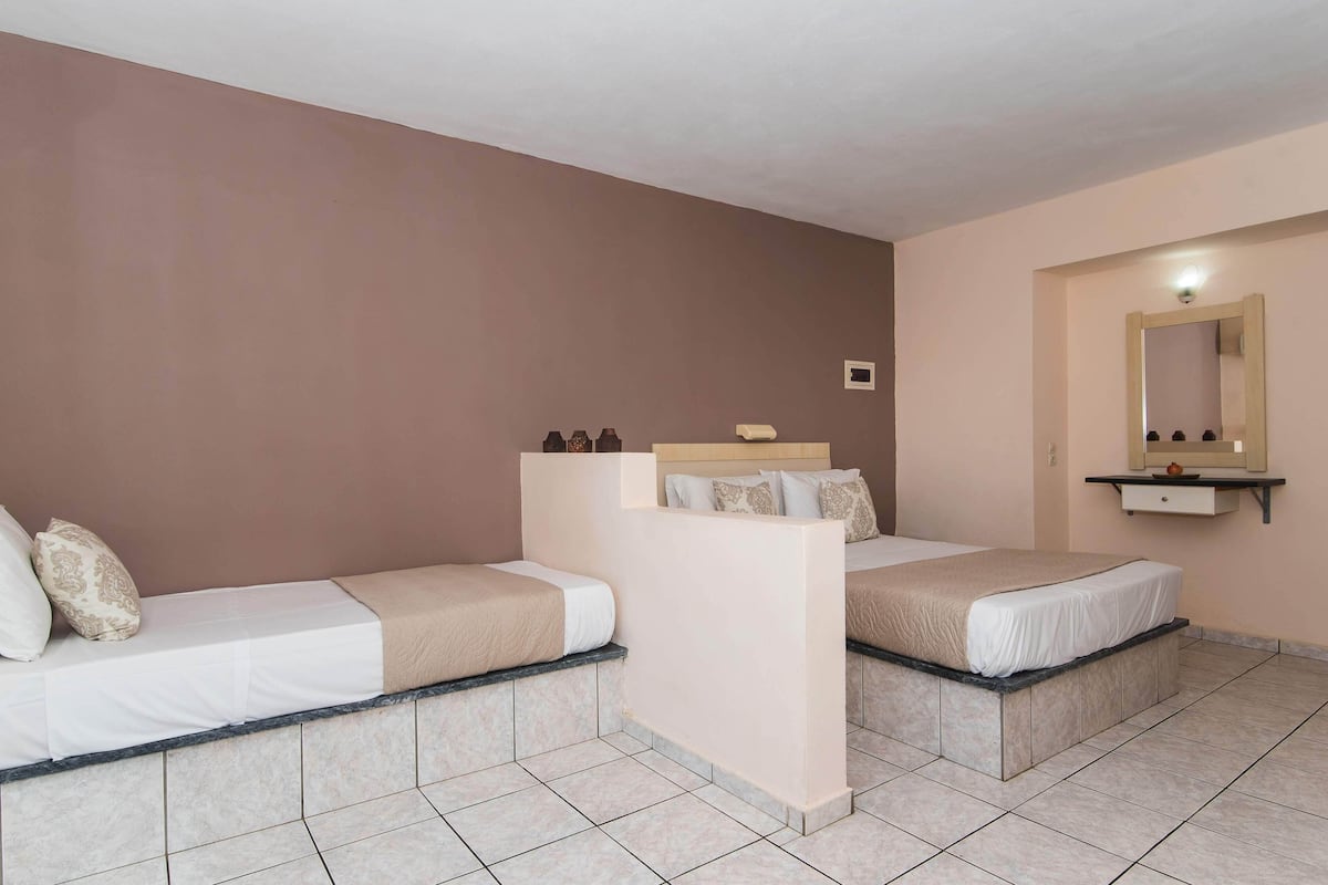 A hotel room with two beds, a small shelf with toiletries, and a mirror above the shelf.