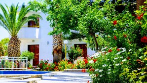 A white building with a balcony, surrounded by lush greenery and flowering plants. - Aspro Hotel (Hersonissos)