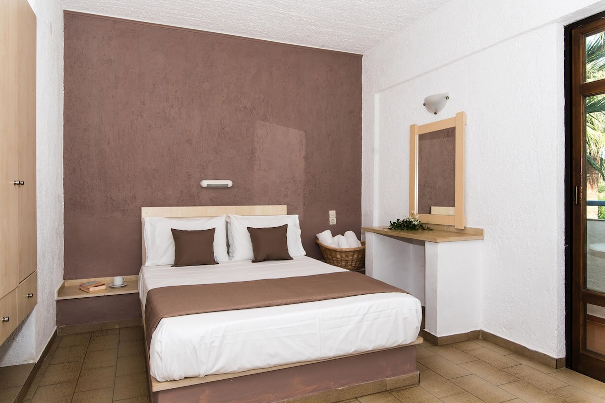 A bedroom with a bed, a nightstand, a bedside table, a mirror, and a window.
