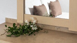 A mirror with a wooden frame reflecting a bed with white and brown pillows, a nightstand, and a wall with a textured finish. - Aspro Hotel (Hersonissos)