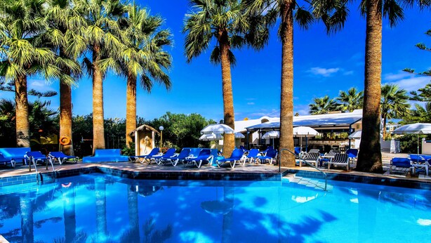 A clear blue pool surrounded by palm trees and blue lounge chairs. - Aspro Hotel (Hersonissos)