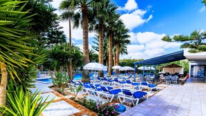A poolside area with blue lounge chairs and umbrellas, surrounded by palm trees. - Aspro Hotel (Hersonissos)
