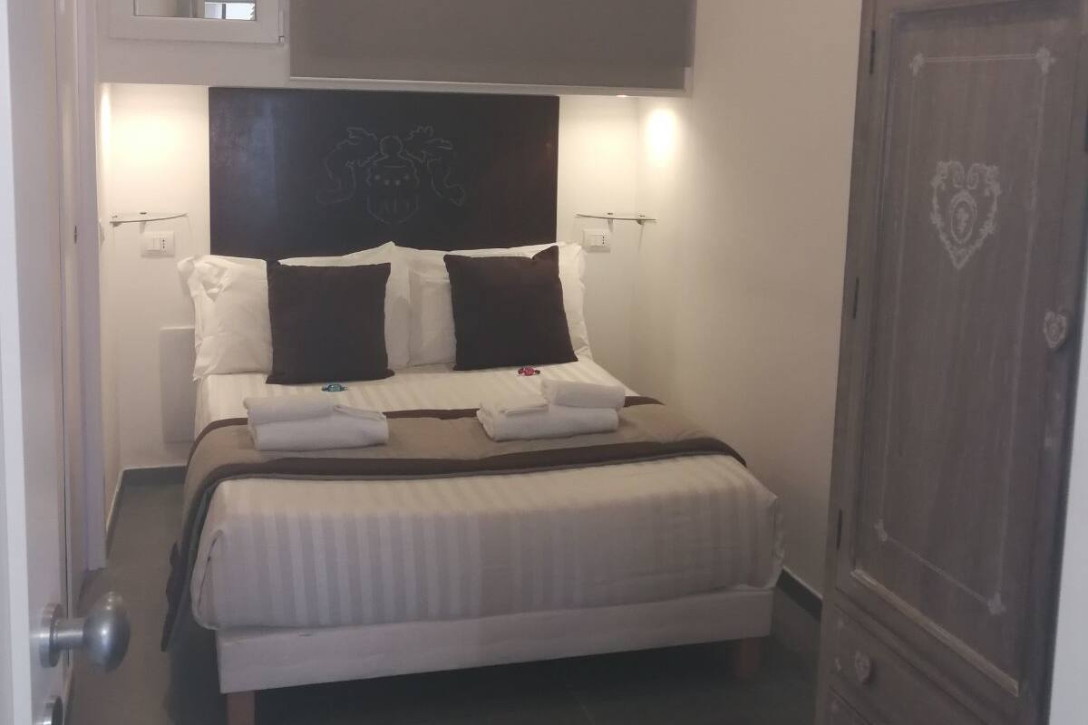 A neatly made bed with pillows and a blanket, a large wardrobe, a mirror, and a wall-mounted projector.