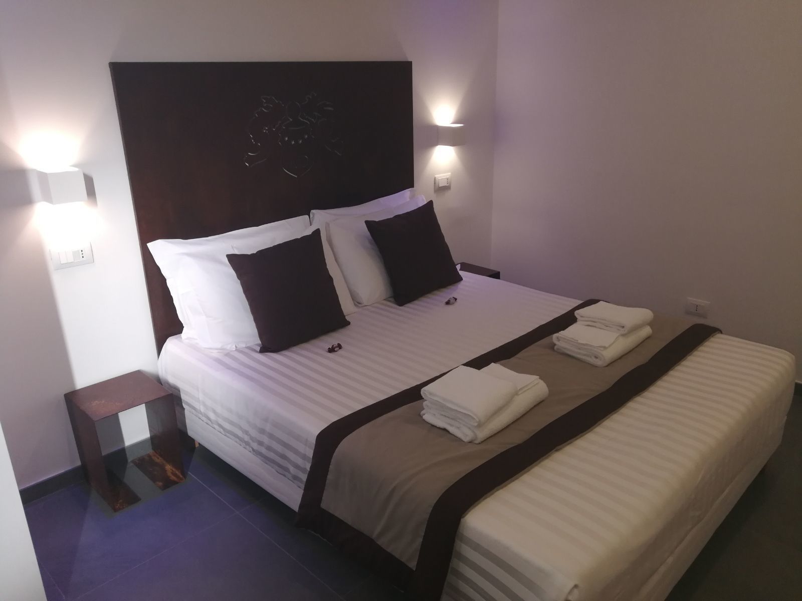 A neatly made bed with white and dark pillows, a striped bedspread, and two folded towels on the footboard.
