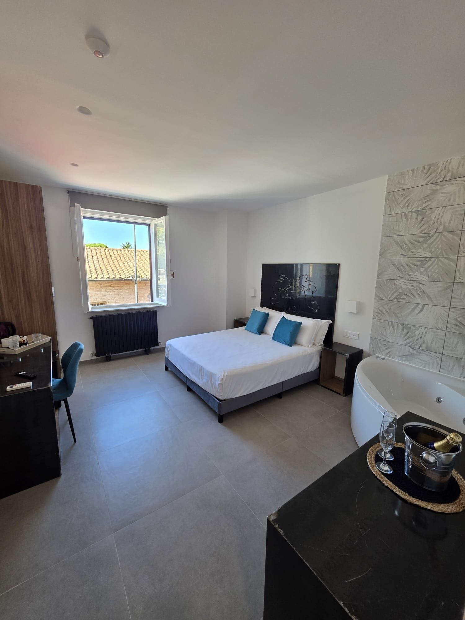 Une chambre d’hôtel comprenant un lit, un bureau, une chaise, une fenêtre, un radiateur, une œuvre d’art accrochée au mur et une baignoire.