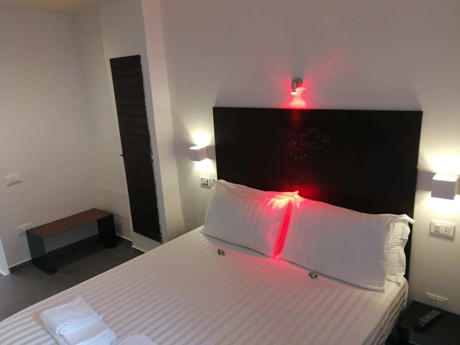 A hotel room with a bed, bedside lamps, a nightstand, and a bench.