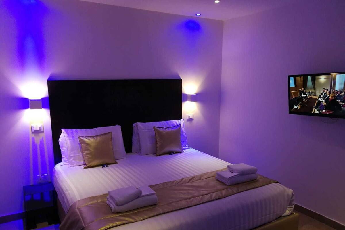 A hotel room with a large bed, two bedside lamps, a flat-screen TV, and a small side table.