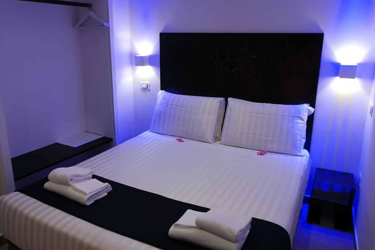 A neatly made bed with white linens and pillows, a black headboard, and two bedside lamps.