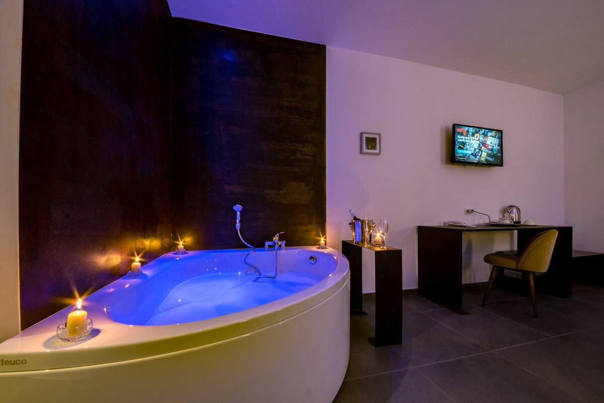 A modern bathroom with a large bathtub, a small desk, and a television.
