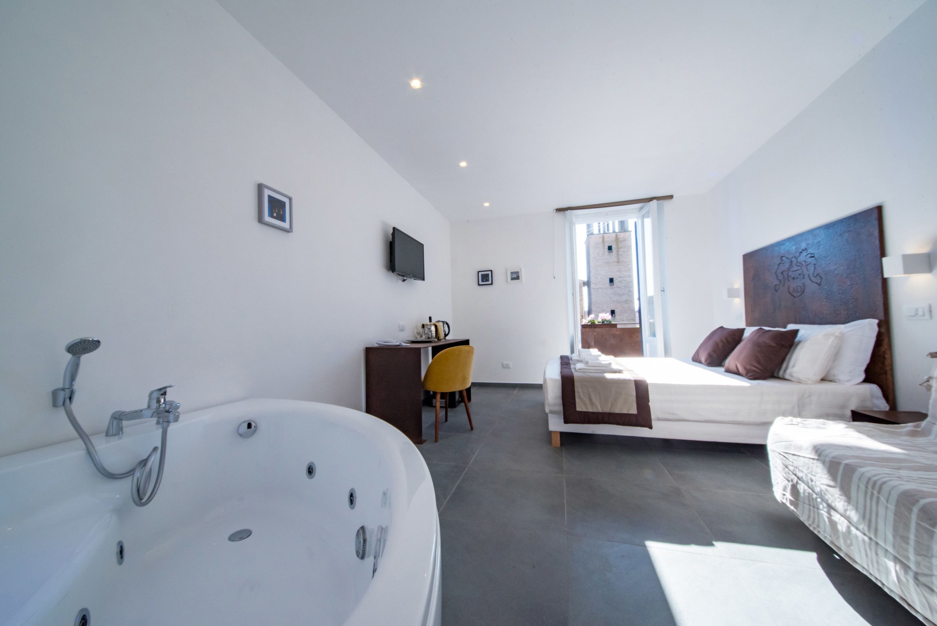 Camera d'albergo moderna con una grande vasca da bagno, un letto con molti cuscini, una scrivania con una sedia e un'ampia finestra.