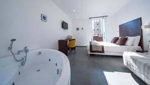 A modern hotel room with a large bathtub, a bed with multiple pillows, a desk with a chair, and a large window. - Assisivm Antica Dimora AD (Assisi)