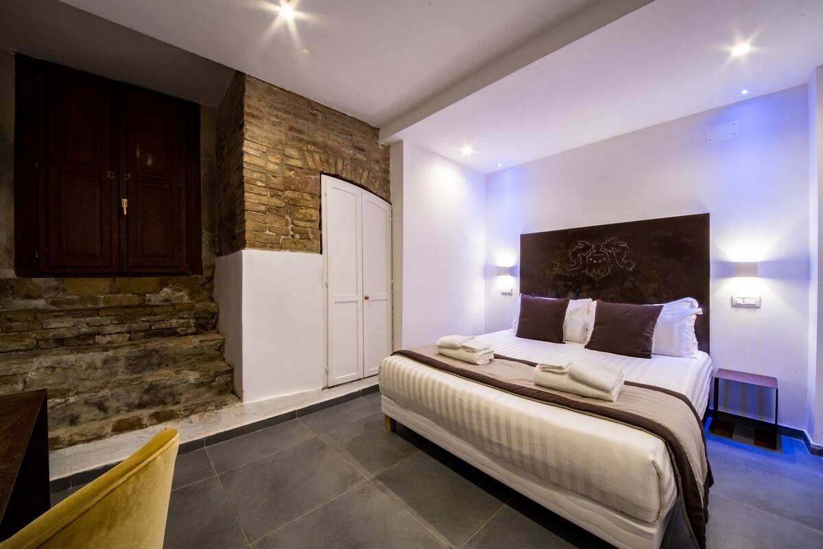 A bedroom with a stone accent wall, a large bed with pillows, and a wardrobe.