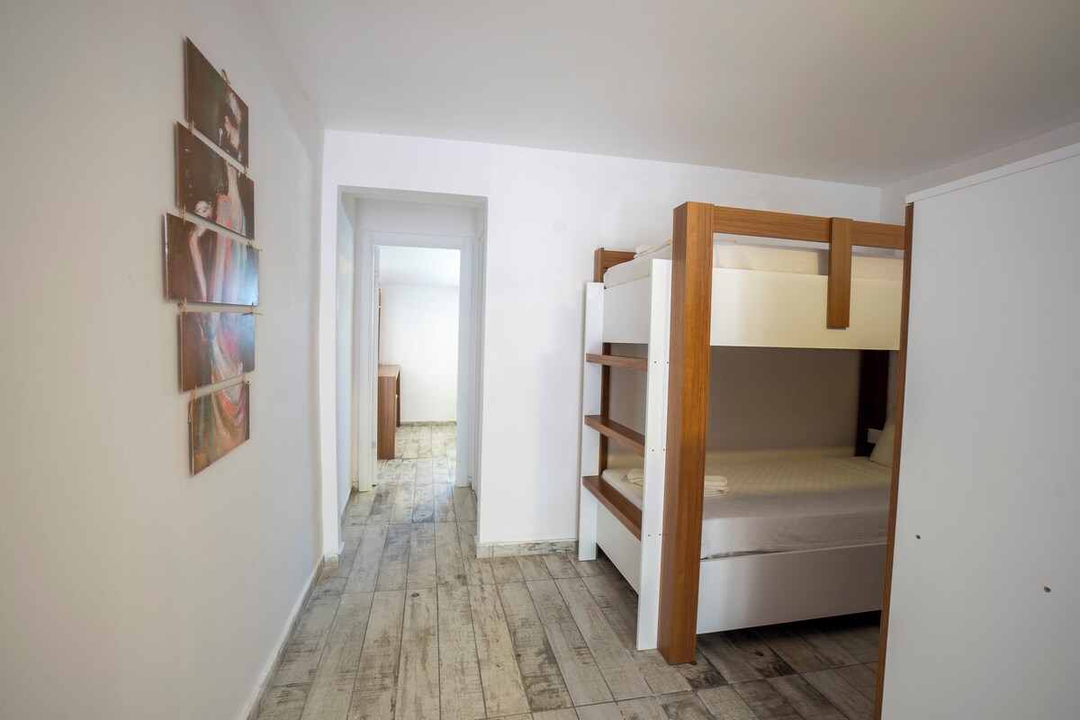 A room with a bunk bed, a hallway with a door, and a wall with framed pictures.