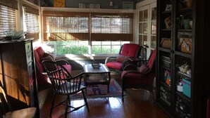 Une pièce chaleureuse avec des fauteuils en osier, une table en bois et une bibliothèque remplie de divers objets.