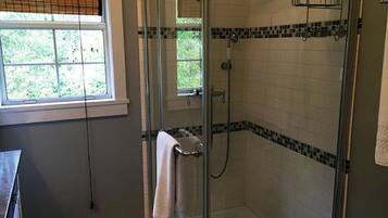 A glass-enclosed shower with a towel rack, a window with blinds, and a tiled wall with a black and white border.