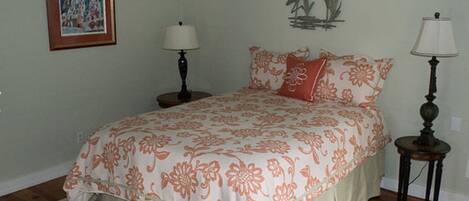 Une chambre à coucher avec une couvre-lit à motifs floraux, un tableau encadré au mur et deux lampes.